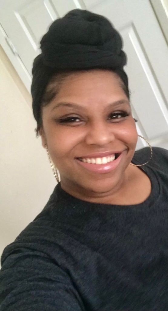 Beautiful brown skin woman with black head wrap and shirt smiling,